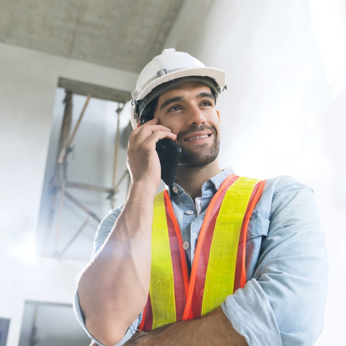 portrait of young caucasian male engineer wearing uniform and hard hat hand use smartphone communication in site construction background